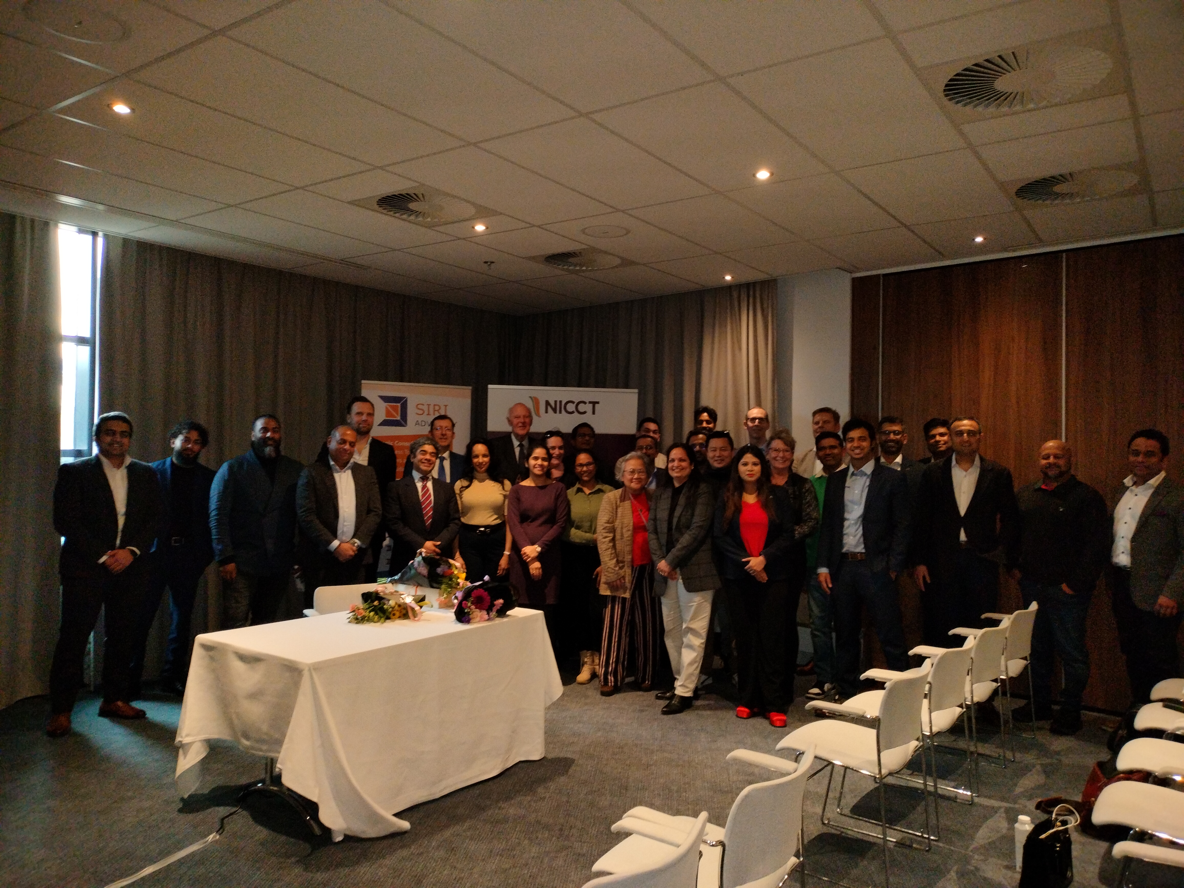 Guests of the NICCT Synergy Series networking event in front of Siri Advisory and NICCT banners